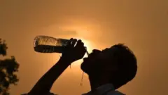 A man drinks water from a bottle in front of a hot Sun