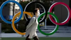 A woman wearing a protective mask walking in front of Olympic rings at the Olympics Museum in Tokyo