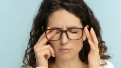 Una mujer con lentes se frota los ojos.