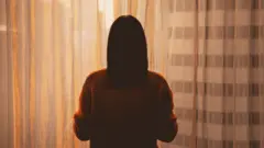 Sombra de mulher, de costas para câmera, olhando para fora da janela