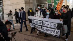 香港「反送中8·18未經批准集結」案被告人進入西九龍法院大樓應訊前展示抗議標語（16/2/2021）