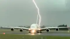 ایمریٹس کے طیارے کے پیچھے کچھ فاصلے پر آسمانی بجلی گرنے کا منظر دیکھا جا سکتا ہے