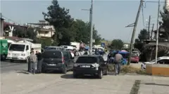 sokakta park etmiş araçlar ve kenarda durup bakan insanlar
