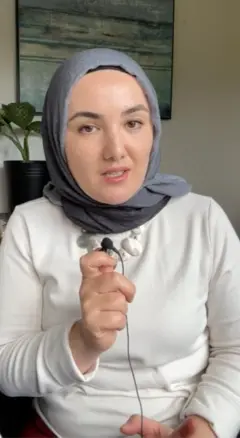 Boshlovchi Hulkar Nuritdin mikrafon ushlab kameraga gapiryapti. Uning egnida oq kuylak, boshida kul rang hijob.
