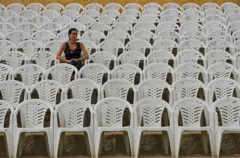 Mulher sentada, rodeada de cadeiras monobloco