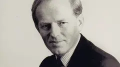 Foto em preto e branco de John Smyth vestindo camisa listrada e terno escuro