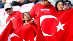Siyah bir Türk bayraklı kadın Türkiye'nin maçında milli oyuncular desteliyor. Yanında ona bakan biri var