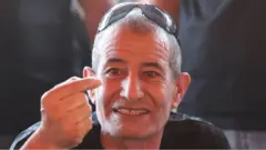 Kaid Farhan Elkadi sa sunčanim naočalama na glavi gestikulira rukama i gleda u kameru