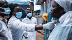 Une équipe de l'ONG locale Shining Hope for Communities (SHOFCO) mesure la température corporelle d'une femme alors que l'ONG installe des stations de lavage de mains dans le bidonville de Kibera à Nairobi, le 18 mars 2020