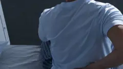 Pessoa sentada na cama tocando a lombar com a mão