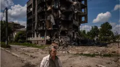 Ukrayna savaşında zarar gören bir binanın enkazı önünde bir kadın