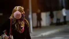 A woman wearing a protective face mask and earmuffs crosses the street during the outbreak of the coronavirus disease) in Beverly Hills, California, US, November 20, 2020