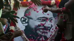 Retrato de Mahatma Gandhi con manos tirándole pétalos de flores