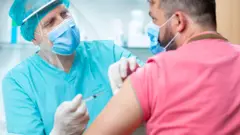 Medic administers jab to man in pink shirt