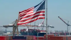 The US flag flies over a container ship unloading it's cargo from Asia, at the Port of Long Beach, California on 1 August 2019