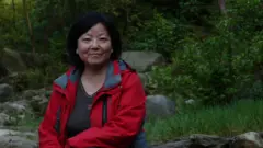 Chinese writer Fang Fang poses in red coat outside.