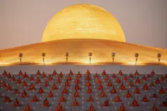Monges rezando em frente à cúpula dourada do templo Wat Phra Dhammakaya, na Tailândia