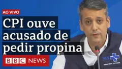 Foto de Roberto Dias usando camisa branca e colete do Ministério da Saúde, acompanhada do seguinte texto: Ao vivo - CPI ouve acusado de pedir propina