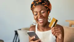 Une jeune femme utilisant une carte de crédit et un smartphone chez elle