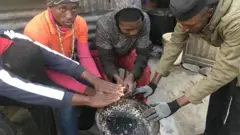 Some group of young men dey warm dia hands for fire.