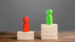 Em mesa, duas pilhas de peças (como se fossem de dominó) com diferentes alturas e dois bonecos no topo — representando os votos de dois candidatos diferentes