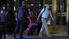 Dois policiais fazem escolta de casal de turistas carregando malas em frente a hotel