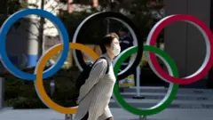 Woman in mask walks past Olympic rings