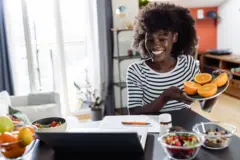 Une nutritionniste joyeuse et diversifiée montre à sa cliente, lors d'un rendez-vous virtuel, des fruits et légumes sains, des compléments alimentaires et des suppléments vitaminiques destinés à la santé et à l'alimentation.
