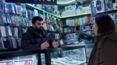 یک کارگر مغازه در وولویچ در حال پاسخ به سوال خبرنگار بی‌بی‌سی است. او انتقال پول برای قاچاقچیان انسان را تکذیب کرده است. 