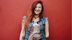 Mariana Torquato sorrindo em frente a parede vermelha