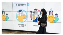 A woman wearing a mask walks past a displayed 'Citizen Behavior Instruction' in Seoul