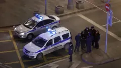 مجموعة من رجال الشرطة يقفون بجوار سيارتي شرطة.