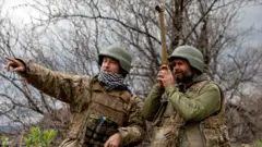 Ukrainian service members talk as one of them uses a periscope at a position