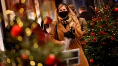 Mujer con mascarilla entre árboles de Navidad