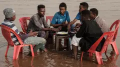 Sudanese men share a meal in the shallows waters of the Tuti island, where the Blue and White Nile merge in Khartoum, on June 24, 2019.