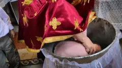 A Romanian Orthodox priest immerses a baby's head during a baptism (file pic)