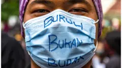 Pengunjuk rasa mengenakan masker saat mengikuti unjuk rasa