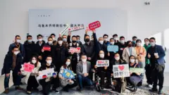 테슬라가 온라인상에 신장 대리점 개점 행사 사진을 올렸다. 사람들이 '테슬라는 신장을 사랑한다(Tesla Loves Xinjiang)'고 적힌 팻말을 들고 있다