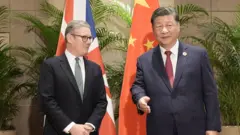 身穿西服的施紀賢爵士(左)與習近平(右)在巴西里約熱內盧G20峰會週邊會晤,兩人站在英國與中國國旗前合照(18/11/2024)