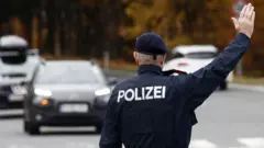 Un officier de police autrichien fait des gestes en direction des automobilistes à un point de contrôle de la circulation à Klagenfurt, en Autriche