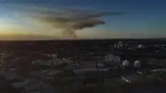 Vista aérea de Cuiabá, com alguns prédios se destacando, e fumaça ao fundo