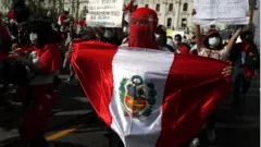 Una manifestante con una capucha y una bandera de Perú.