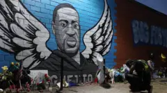 Un homme à genoux devant un mémorial et une peinture murale pour George Floyd