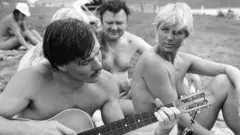 Eine Gruppe nackter Menschen, die Gitarre spielen