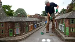 A man sweeps the ground in the middle of a street in a model town