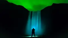 A waterfall is illuminated under the aurora lit sky