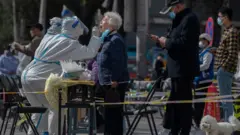 A health worker wears protective gear as she gives a nucleic acid test to detect COVID-19 on a local resident at a mass testing site after new cases were found, on April 6, 2022 in Beijing, China.
