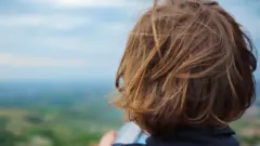 Child with long hair, seen from behind, looking at a landscape
