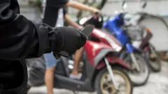 Braço segurando faca, com motos ao fundo