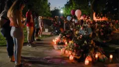 People stand in prayer in front of memorial crosses, for the children who died in the mass shooting at Robb Elementary School, in Uvalde, Texas, U.S. May 27, 2022